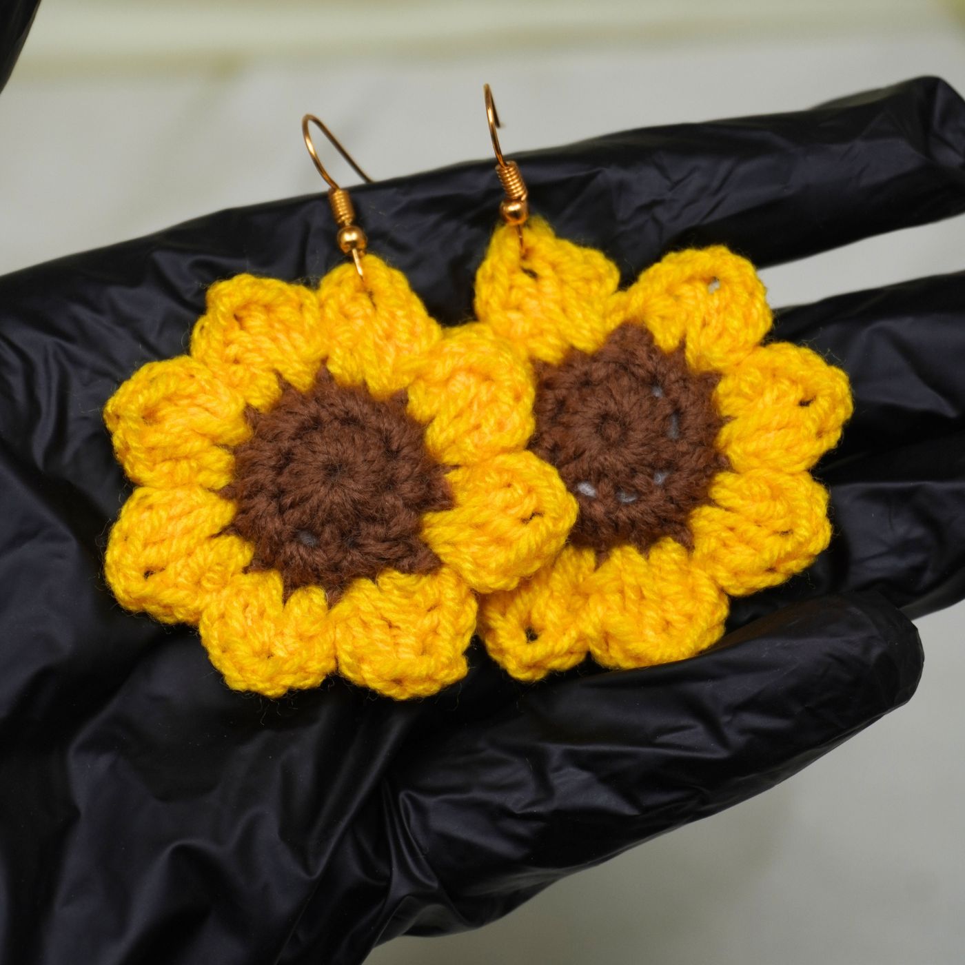 Crocheted sunflower earrings with yellow petals and brown centers on a black surface.
