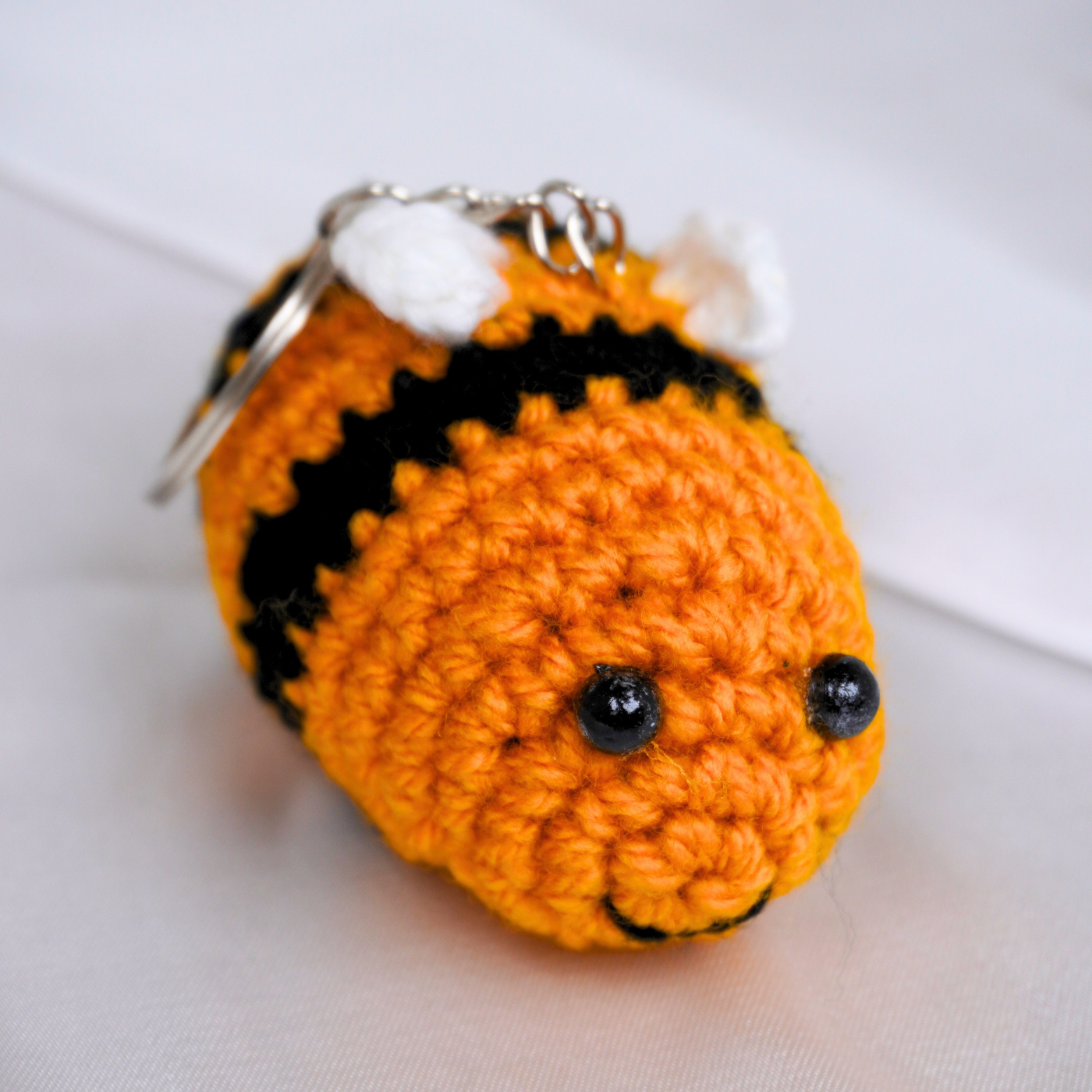Crocheted bumble bee keychain with black details on a white background