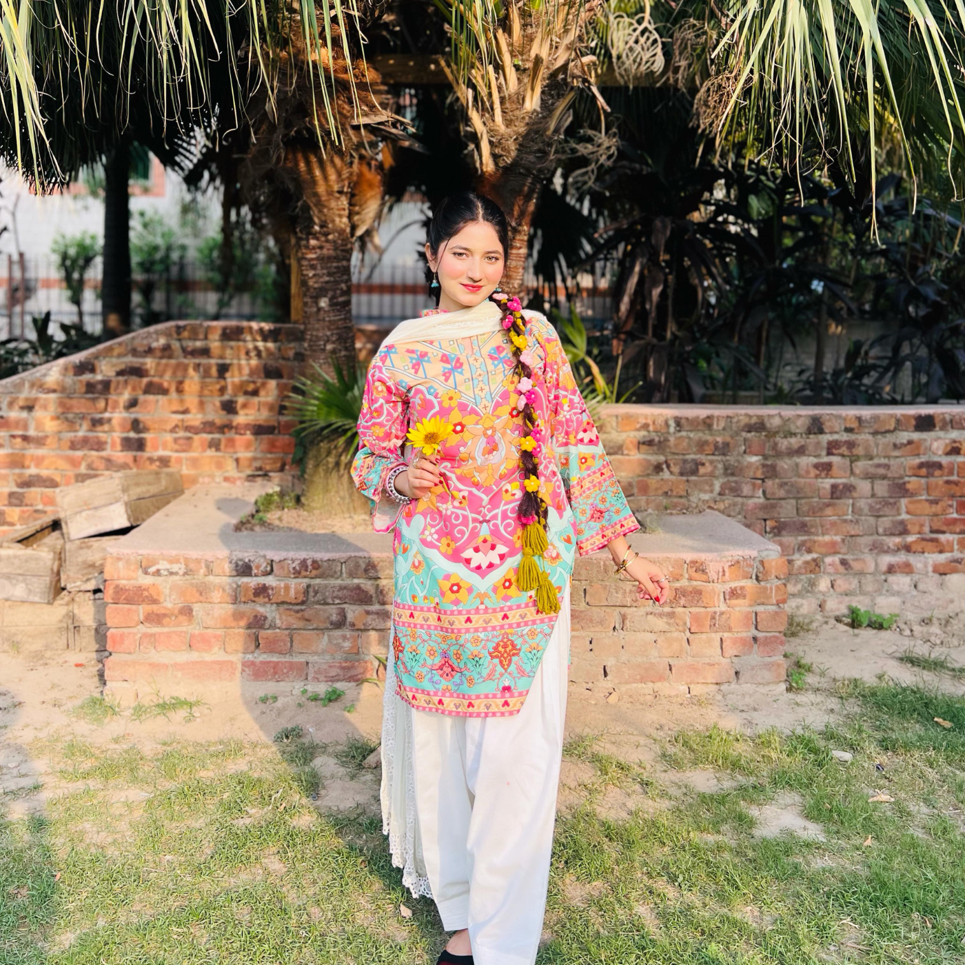 Woman in a colorful traditional Parandi standing outdoors with greenery and brick wall in the background