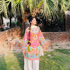 Woman in a colorful traditional outfit standing outdoors with palm trees in the background