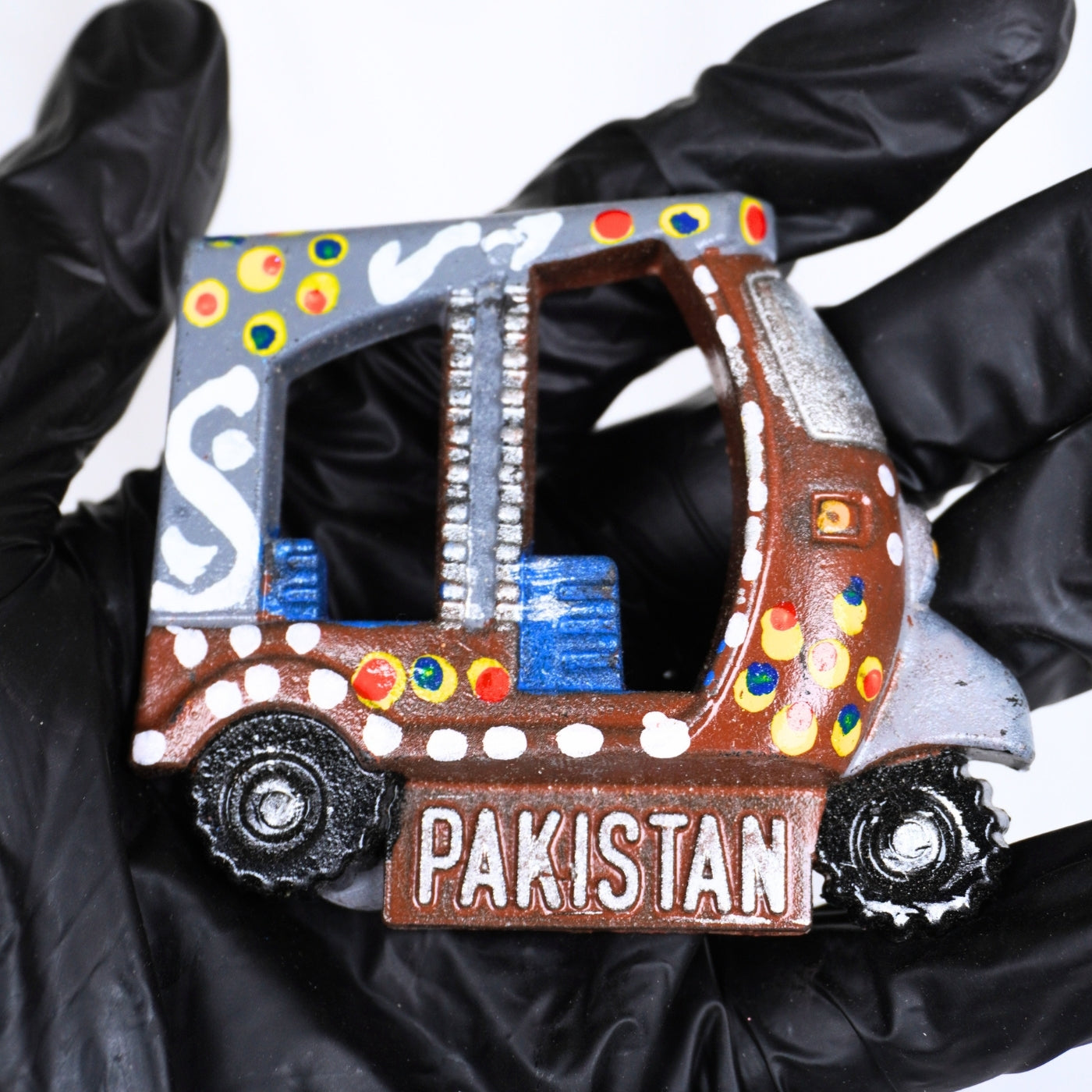 Decorative refrigerator magnet shaped like a truck with 'Pakistan' text, held by a gloved hand.