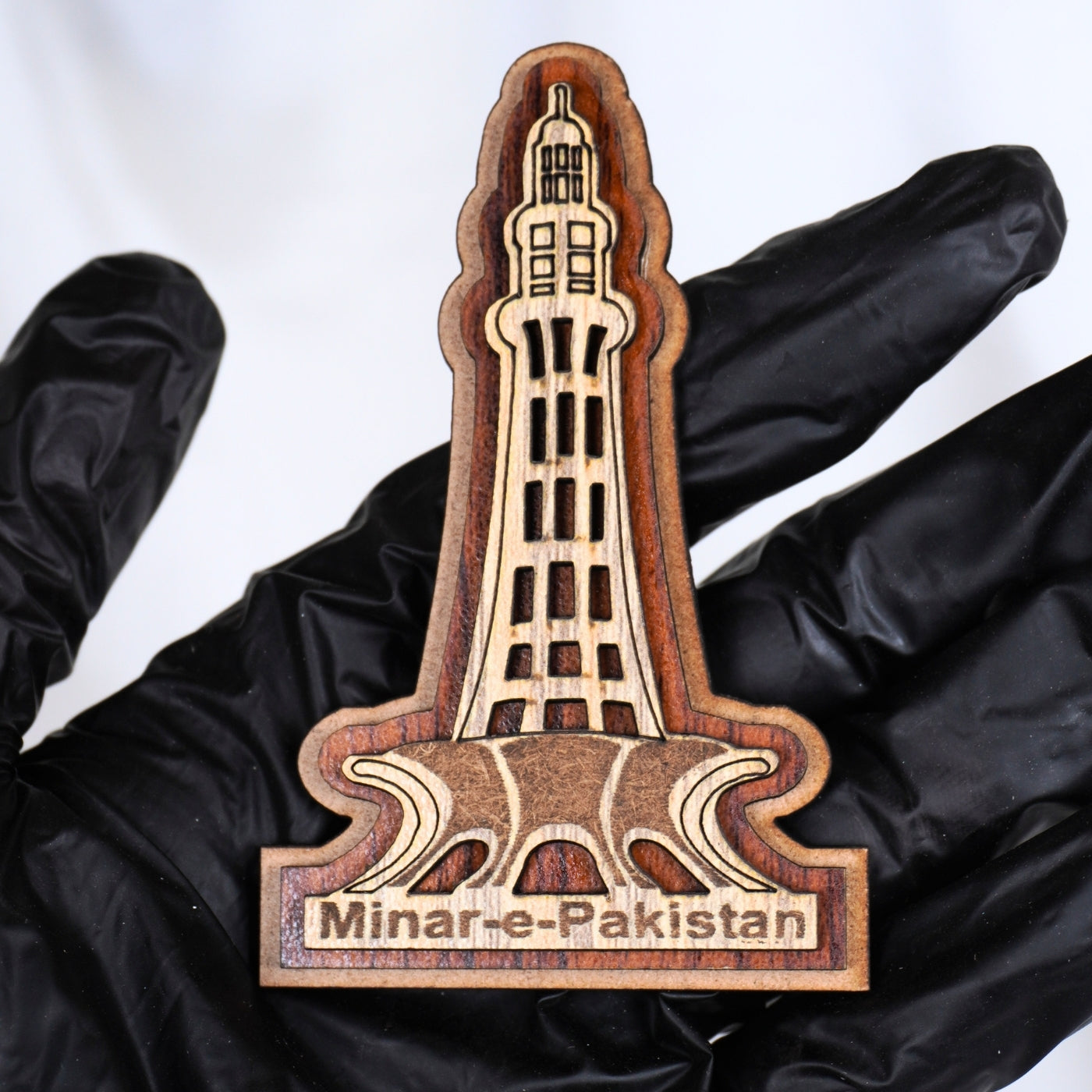Wooden model of Minar-e-Pakistan held by a gloved hand on a white background
