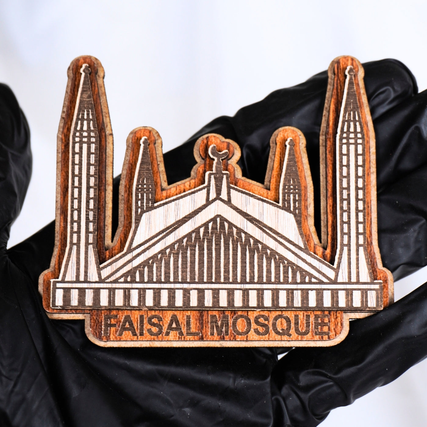 Wooden model of Faisal Mosque held by a person wearing a black garment.