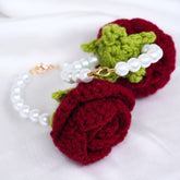Crocheted red rose with green leaves and a pearl bracelet on a white background