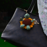 Black handbag with a crocheted turtle keychain on a dark background