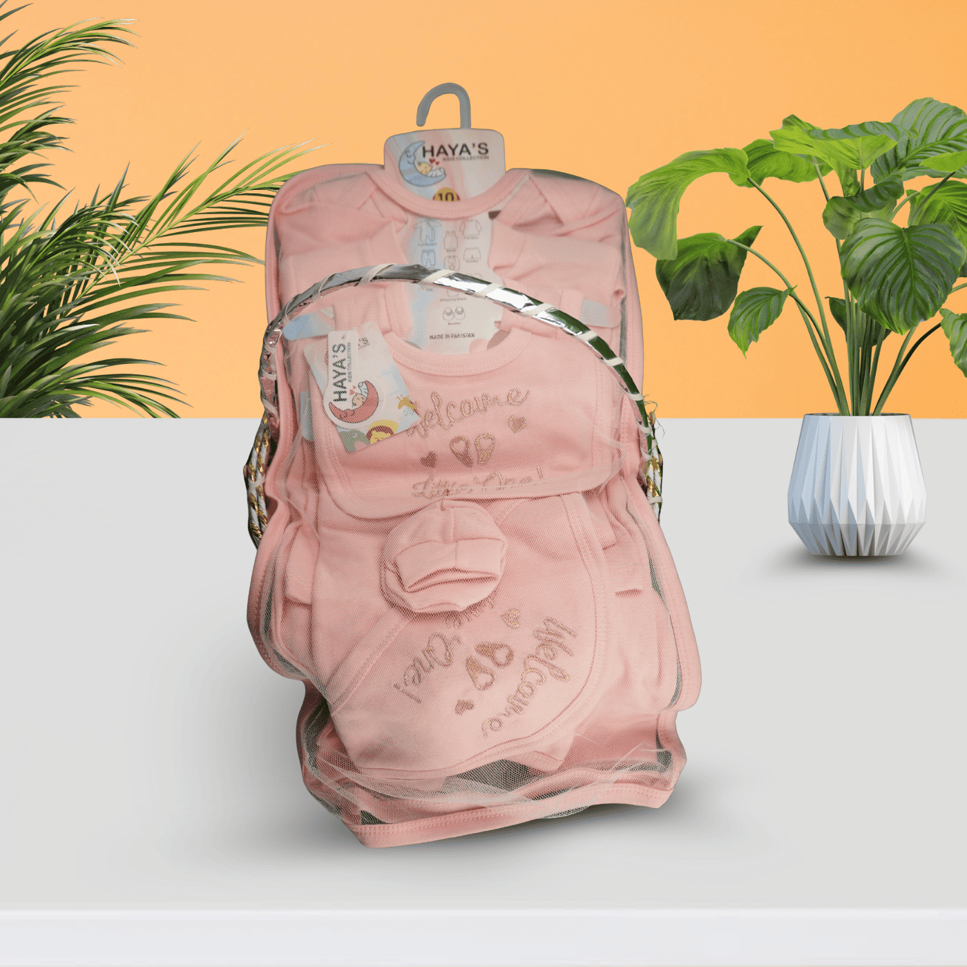 Pink baby carrier with 'Haya's' branding on a white surface with plants in the background