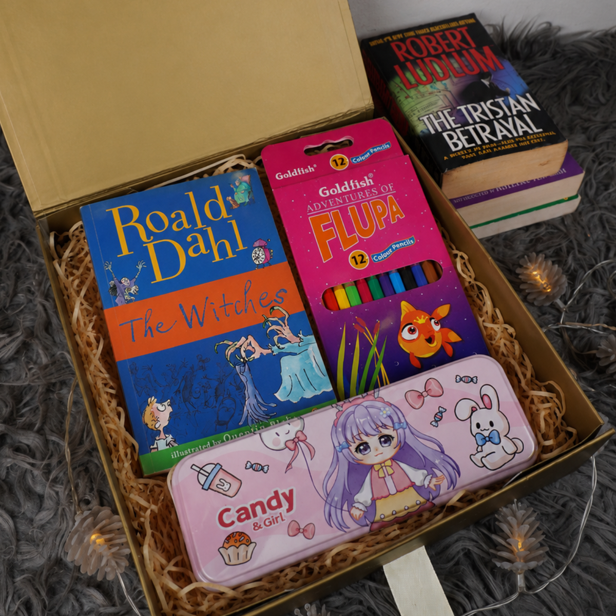 A curated gift box set containing a Roald Dahl 'The Witches' book, a pack of Goldfish 'Open Your Fluka' crayons, and a pink 'Candy & Chilli' pencil case, arranged in a cardboard box with shredded paper.