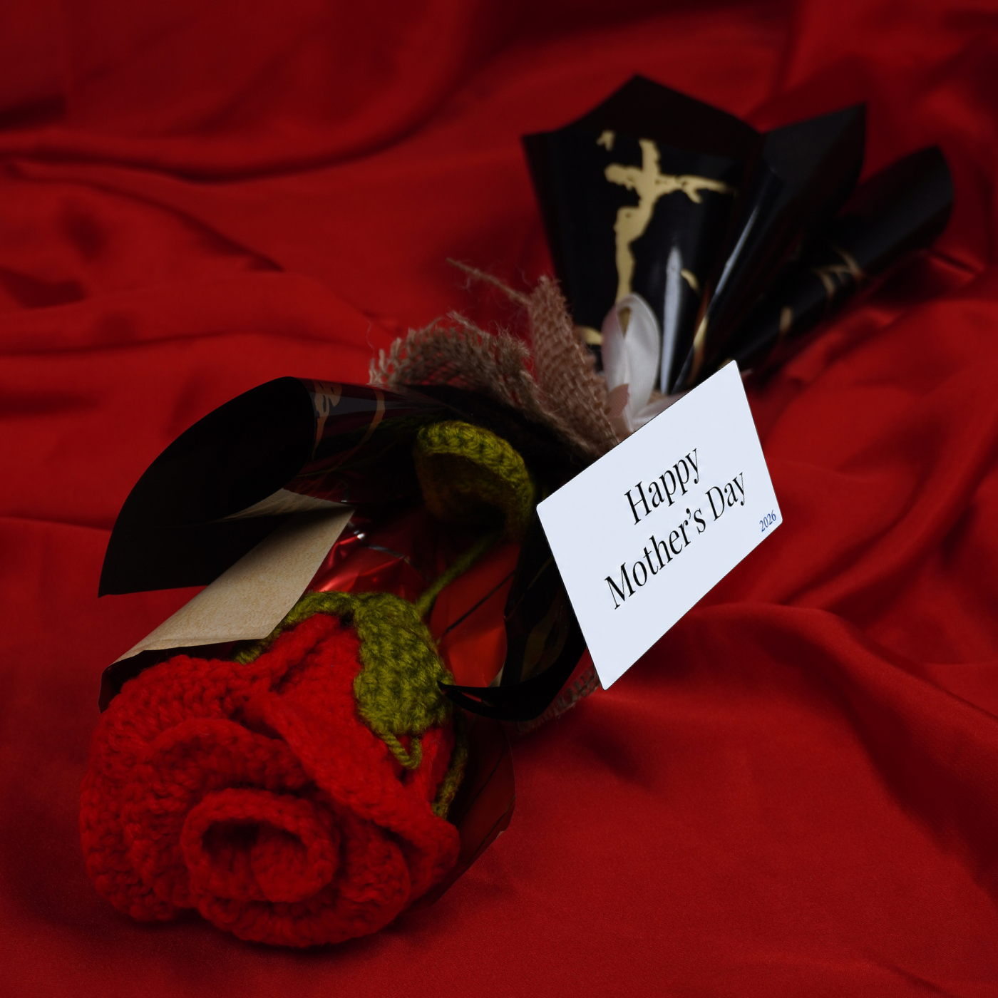 Bouquet with a red rose and 'Happy Mother's Day' card on a red fabric background