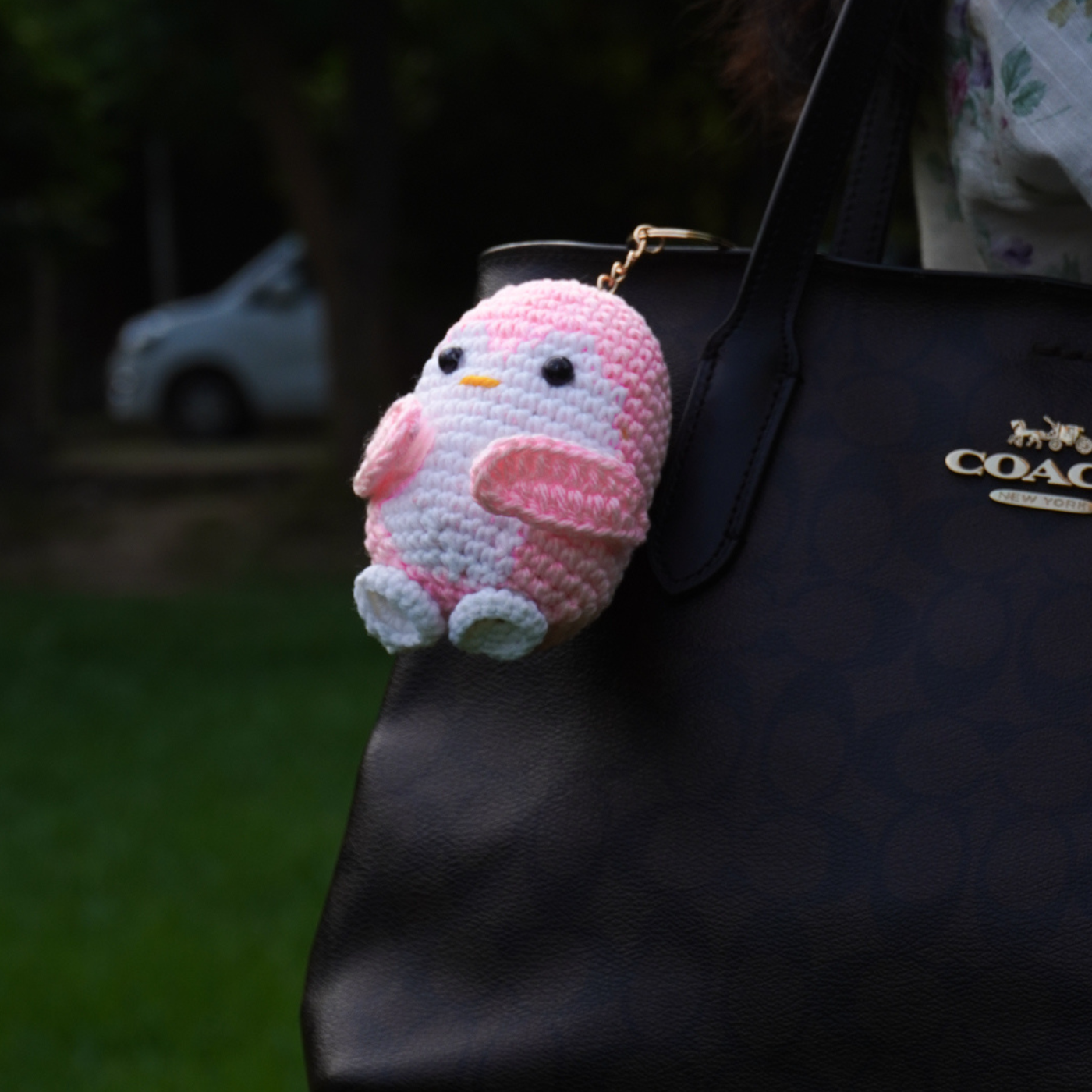 Handmade yellow crochet bee keychain with a "Bee-lieve in you" card hanging on a black Coach bag outdoors in Lahore.