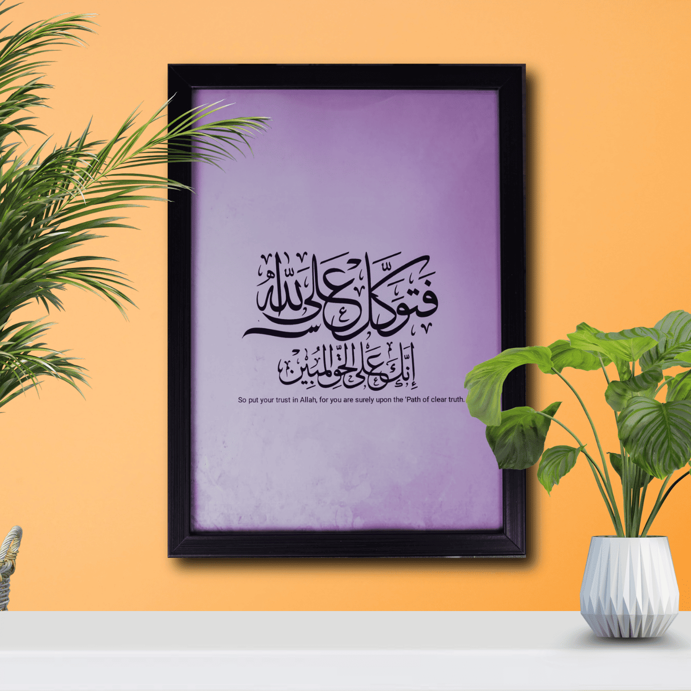 Framed Arabic calligraphy on a purple background with plants on an orange wall.