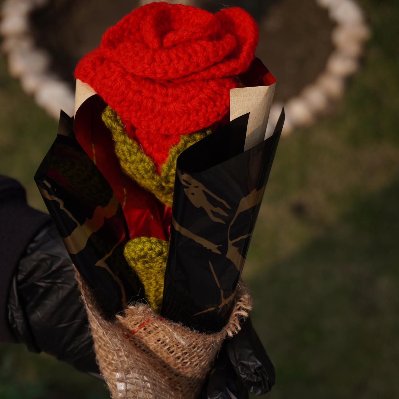 Red knitted flower in a paper cone held by a person with a blurred natural background